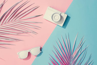 Plaj aksesuarları ve palmiye yaprakları üzerinde pastel pembe ve mavi arka plan, yaz konsepti