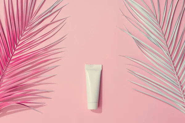 Painted palm leaves and sunscreen on pastel pink background, Tropical summer concept