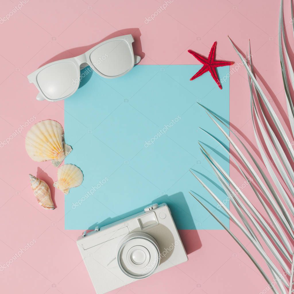camera with beach accessories and palm leaf on pastel pink and blue background, Summer concept   