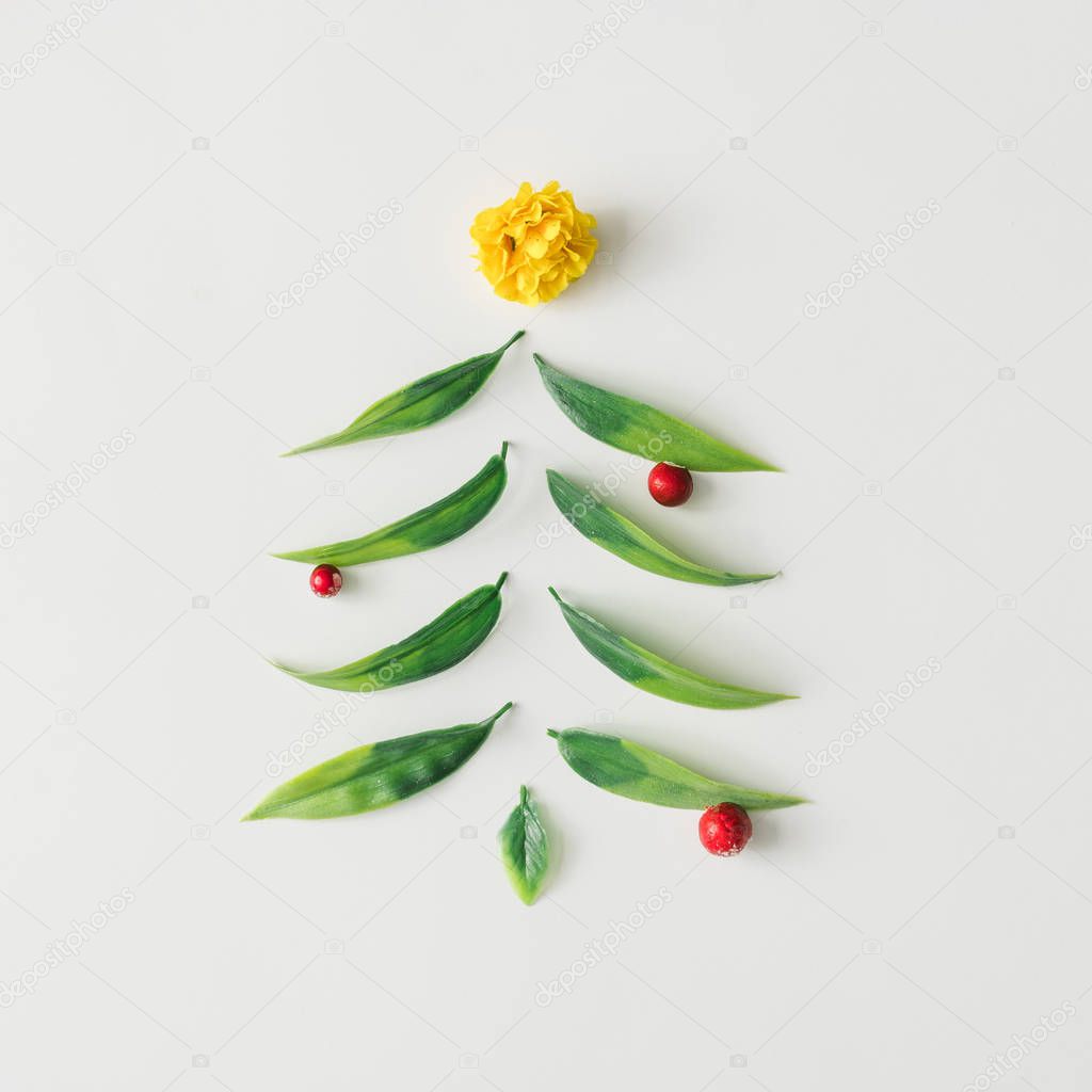 Christmas tree made of green leaves and flower and red berries. Minimal nature inspiration. Flat lay holiday concept.