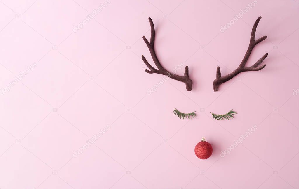 Christmas reindeer concept made of evergreen fir and red bauble decoration and antlers on pastel pink background