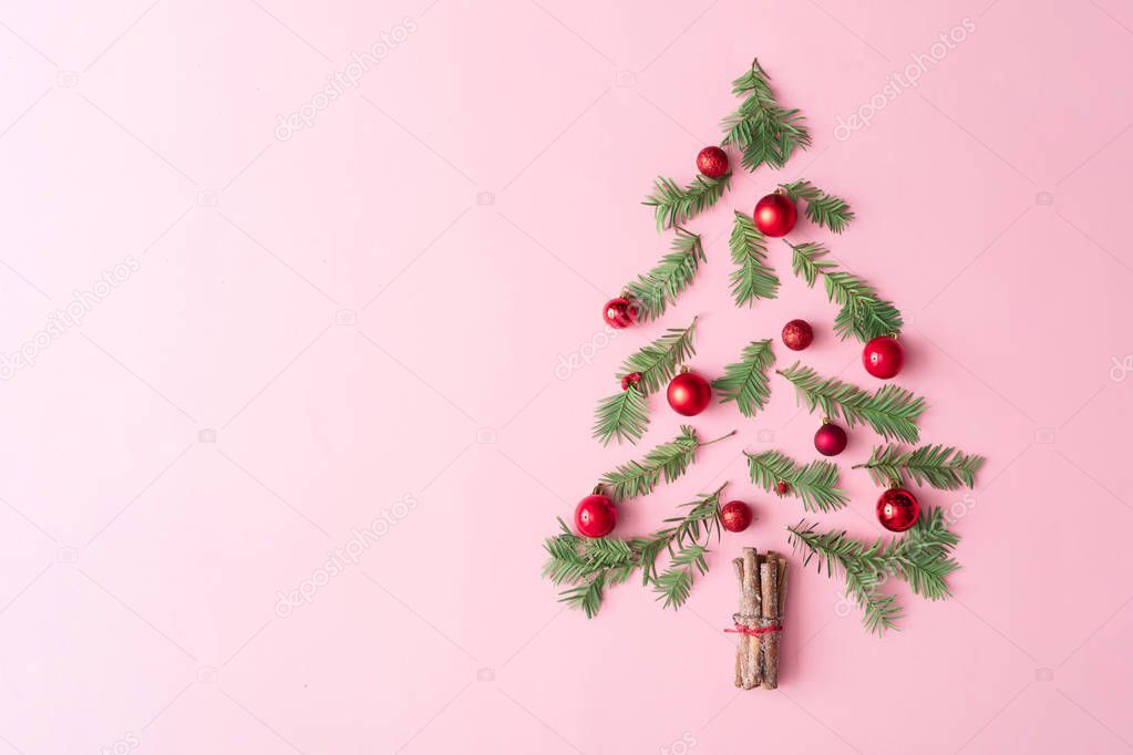 Christmas tree made with evergreen fir branches and bauble decorations with cinnamon sticks on pastel pink background. Minimal holiday flat lay table composition 