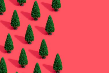 Pastel kırmızı zemin üzerine yeşil Noel ağaçları ile en az kompozisyon desen. Yeni yıl kavramı 