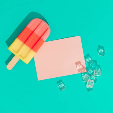 Buz küpleri ve canlı mavi arka plan pembe kağıt kart notu ile dondurma popsicle. Minimal yaz kompozisyonu 