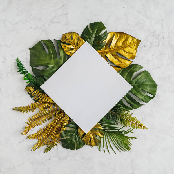 Top view of green and golden tropical palm leaves with white paper card note on marble background. Minimal creative summer concept 