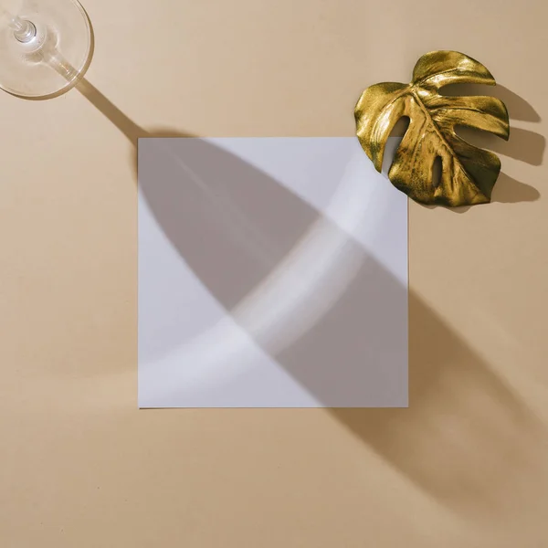 砂のベージュの背景に金色のモンスターの葉と白い紙のカードとシャンパングラスのミニマルトップビュー 夏のクリエイティブコンセプト — ストック写真
