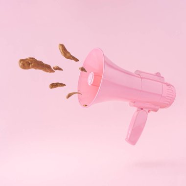 Üzerinde dışkı olan pembe megafon, pastel pembe arka planda. Kötü reklam fikri. Asgari çöp konuşma konsepti.