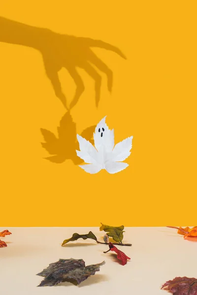 Halloween minimal concept with autumn leaves and witch or zombie hand shadow. Creative spooky ghost. Holiday fun background