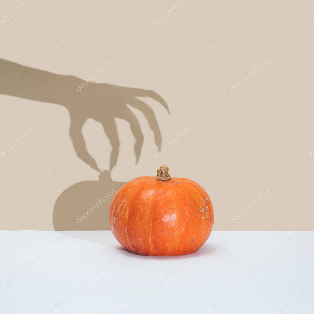 Halloween minimal concept with pumpkin and witch or zombie hand shadow. Creative spooky holiday fun background