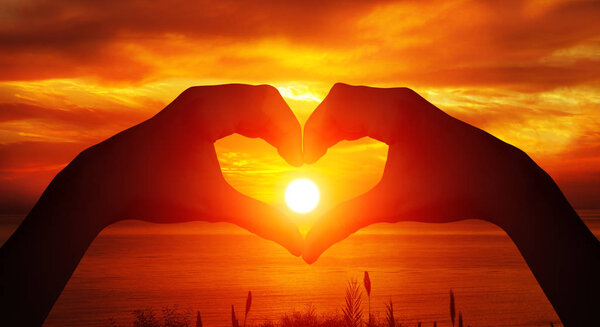 Heart shaped female hands silhouette with sunset background