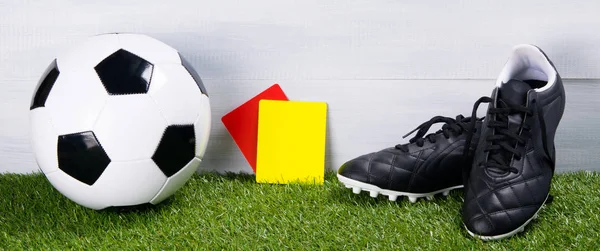 soccer ball, boots, penalty cards for the referee, lie on the grass, on a gray background