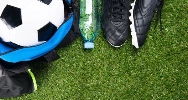 soccer ball in a blue bag, boots, a bottle of water and a sporty T-shirt, against the background of grass
