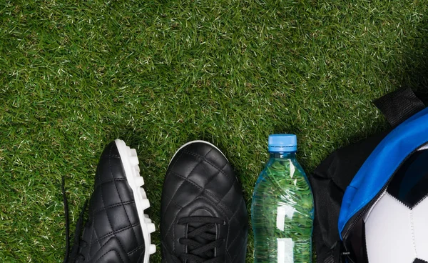 soccer shoes, water bottle and ball in a sports bag on a green lawn