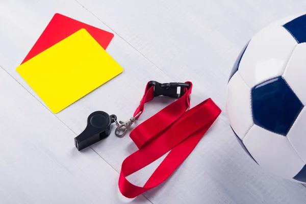 Football ball, two penalty cards and a whistle for the referee, on a gray background