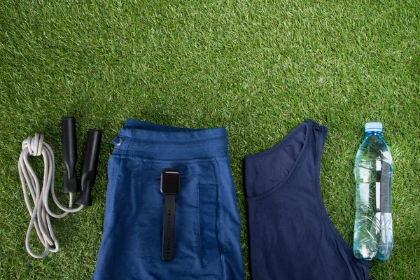 blue sportswear, accessories for fitness and a bottle of water, against the background of grass, on shorts ready for diagnosis of cardio state and pulse, smart clock