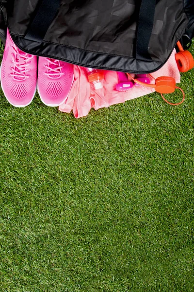 pink clothes and accessories for fitness, a bottle of water, in a black sports bag, on the background of grass, with a place for writing