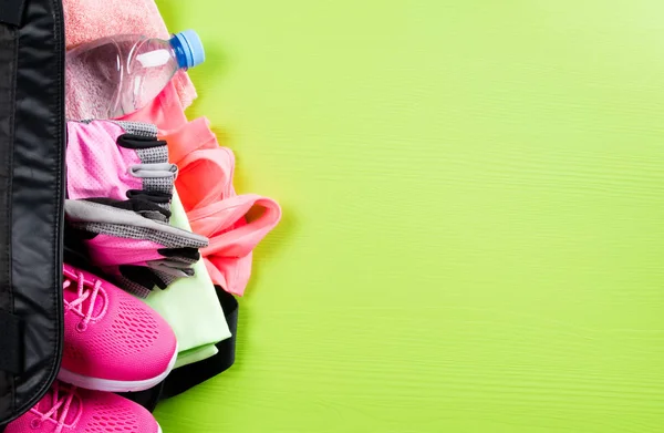 pink sportswear and accessories for fitness, a bottle of water, lie in a black bag, on a light green background with a place for recording