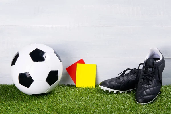 soccer ball, black boots and two penalty cards for the judge, stand on the grass, on a gray background