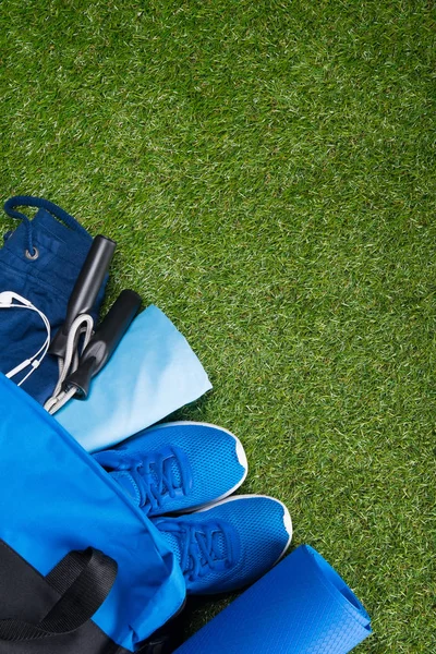 on the green background of the lawn, lies a blue sports bag with clothing and sports equipment for running and jumping high. there\'s room for writing.