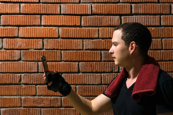 a man in the gym reading a workout plan on a smartphone on a red brick wall background