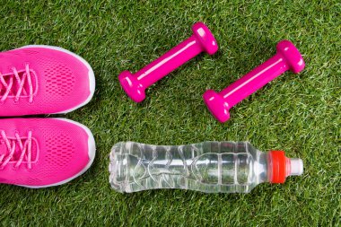 pembe spor spor ayakkabı ve halter fitness ve bir şişe su çim arka planı için