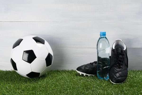 Clean water in a bottle and the concept of football on a green lawn