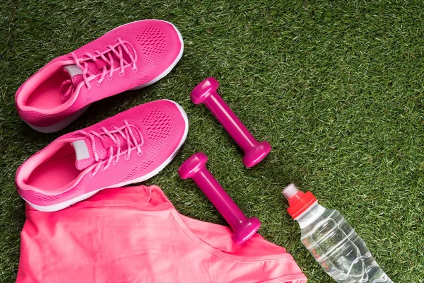 a set of pink sports things for fitness and a bottle of water on a green lawn