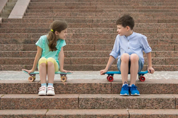 the boy and the girl sort things out, sitting on the steps on the sports boards.