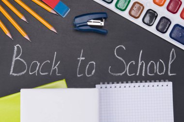 bir siyah üzerine kurulu, tarafından bir tebeşir - tekrar okula ve çevresinde birtakım kalemler ve boyalar, bir yer için bir dizüstü bilgisayar üzerinde bir yazıt ile bir yazıt aşağıda sağda