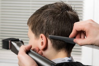 cut hair to the boy using a clipper and comb ////