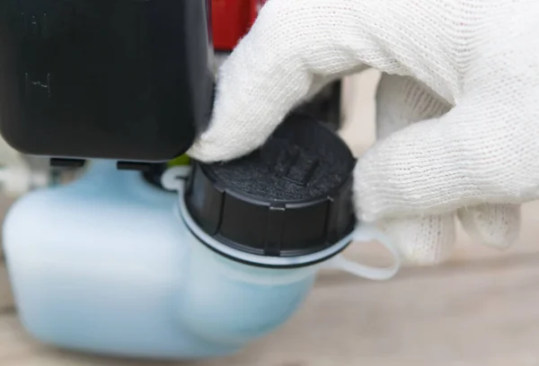 The gloved hand opens the fuel tank cap, two-stroke engine