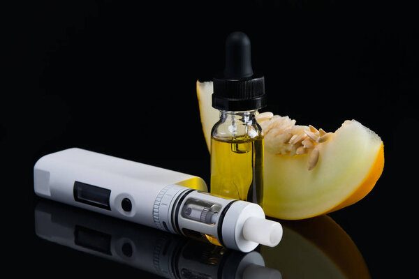 a slice of melon, on a black background, next to the aroma liquid for an electronic cigarette
