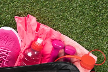 yeşil bir çimenlikte, kadın birtakım şeyler pembe bir şişe su ile açık bir çanta içinde spor