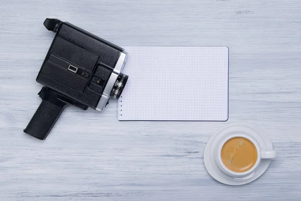 a cup of coffee and an old video camera, lies on a white notepad for writing