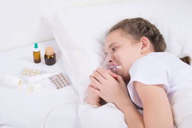yatakta, inhalasyon yapıyor, yatakta bir maske üzerine koyarak ve ilaç-tablet arayan kız