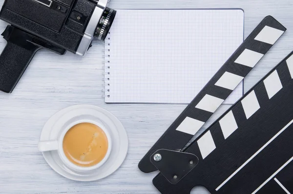 old video camera, frame for shooting, cup of aromatic coffee and a notepad for recording, on a gray background
