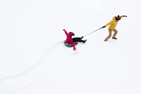 爸爸把女儿卷在白雪上的圆形充气雪橇上 — 图库照片