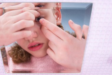 yakın çekim, kız aynaya bakar ve vizyon geliştirmek için lensler koyar