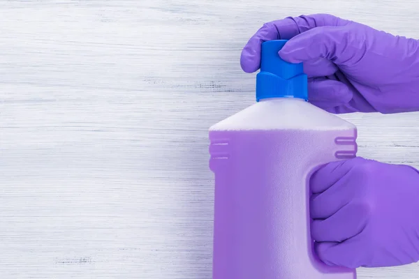 gloved hands open bottle with cleaning agent on gray background