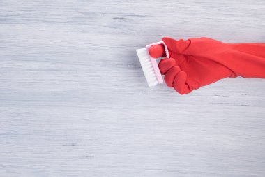 hand in red glove, holds pink brush to clean surfaces on grey background, with space for lettering