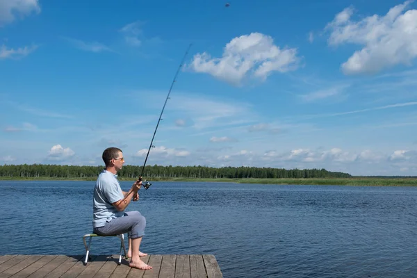 男は桟橋に椅子に座っているし レジャーの湖で魚をキャッチ — ストック写真