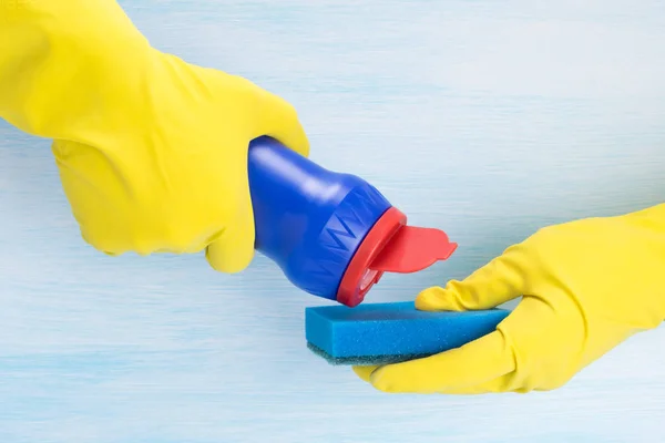 hands in rubber yellow gloves sprinkle cleaning agent on a sponge for cleaning on a light background