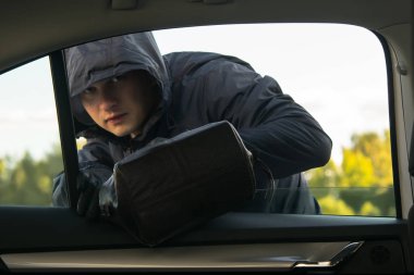 bir adam bir kukuleta ile siyah giysili bir suç işleyen, araba penceresinden bir torba alır