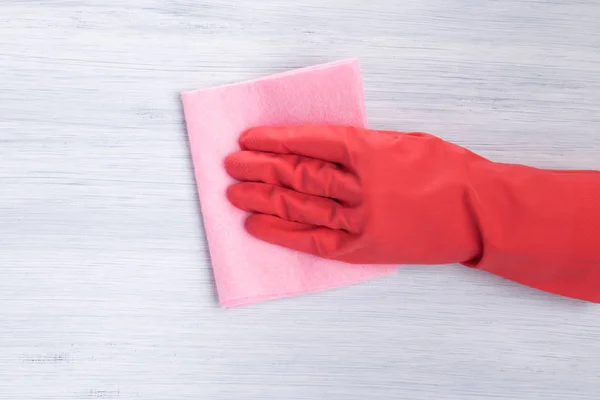 hand in a red glove wipes the surface of a pink rag, close-up, on a light background