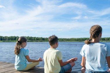 çocuk ve iki kız göl kenarında oturup yoga yapmak