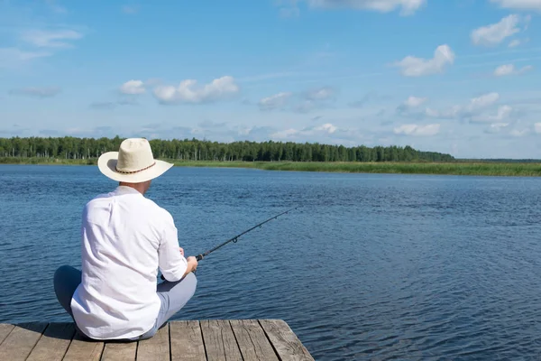 Man Hat Sits Pier Fishing Rod His Hands Looks River — Stock Photo, Image