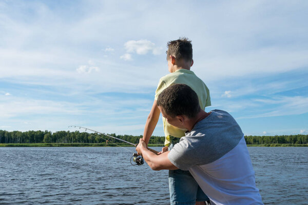 dad teaches son to fish on spinning on the lake, rear view