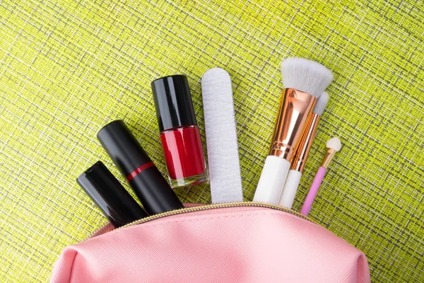 pink cosmetic bag and decorative cosmetics for a makeup of a young woman on a green background