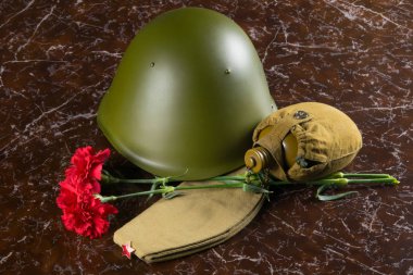 anıtın arka planda, iki kırmızı karanfil, su şişesi, askeri kask ve kap