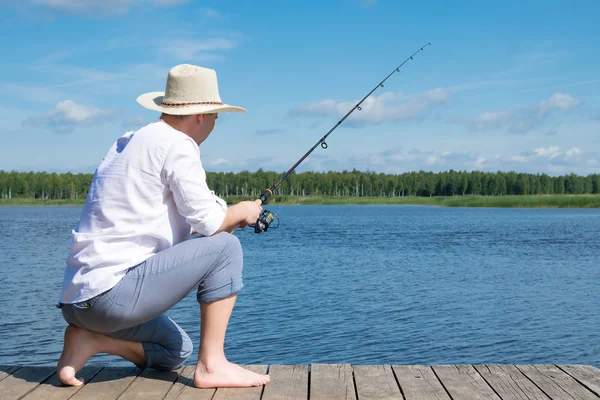白いシャツと帽子をかぶった男が晴れた日に湖で釣りをしている 後ろ見る — ストック写真